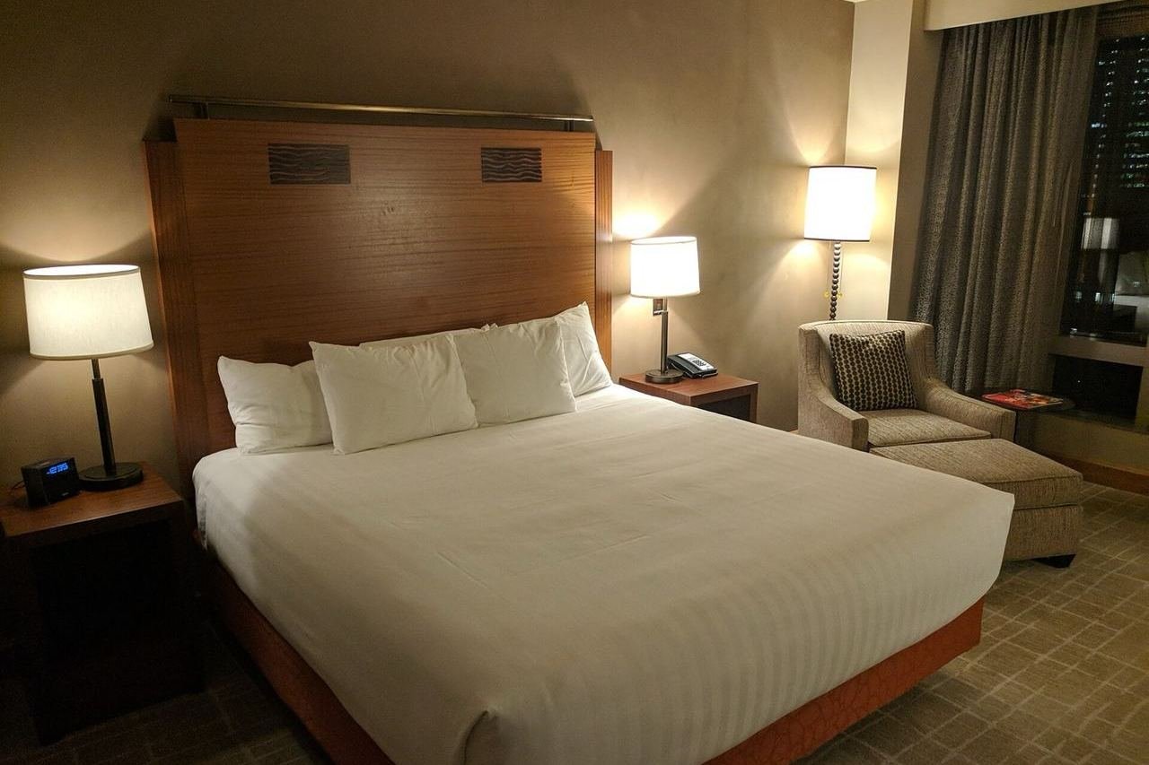 Chambre d'hôtel vide : lit double, tête de lit en bois, tables de nuit et fauteuil.